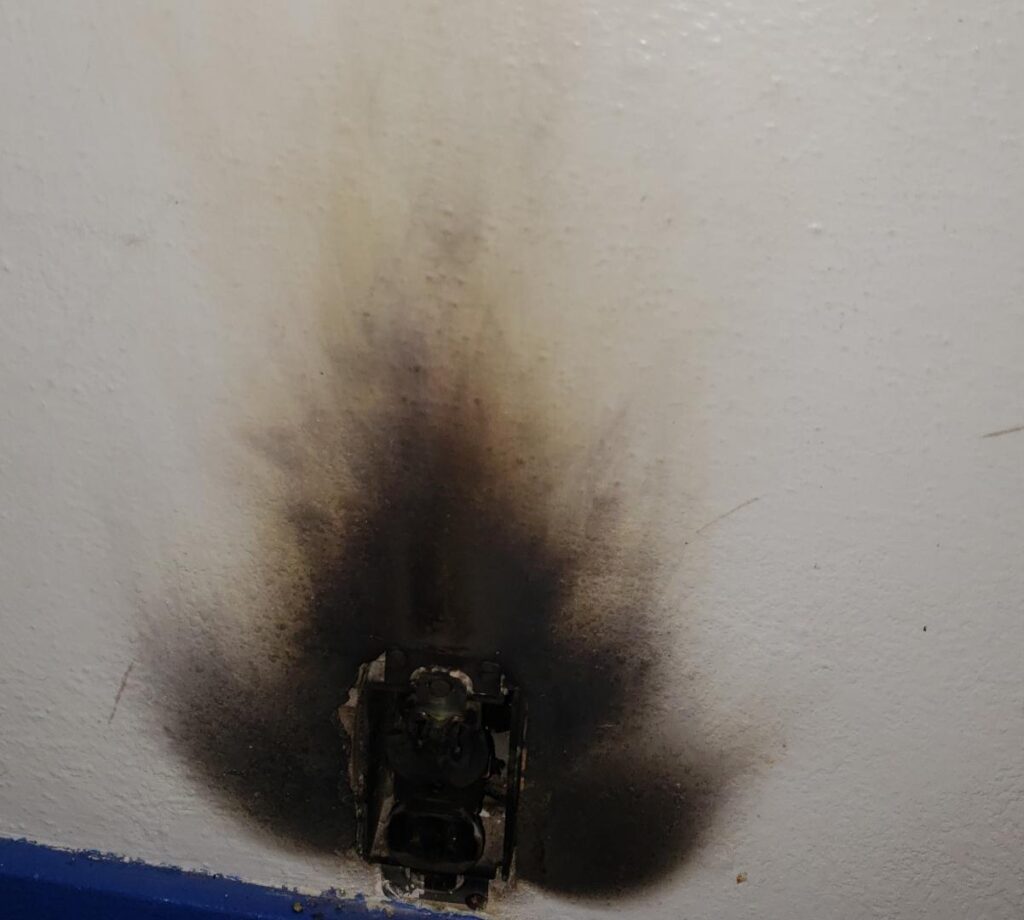 Burnt electrical outlet with black smoke damage on wall by HES