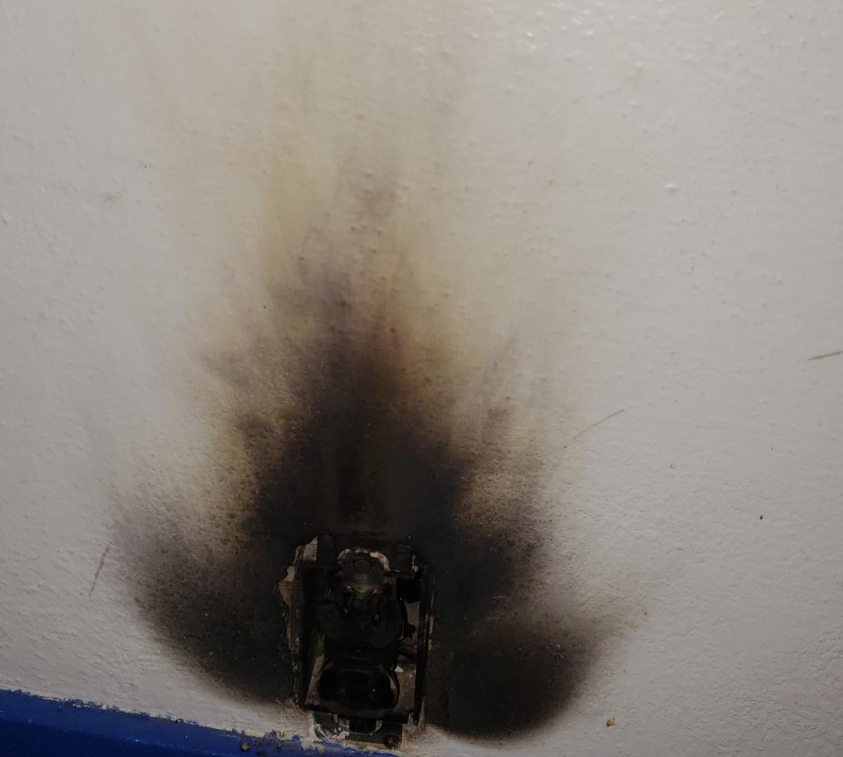 Burnt electrical outlet with black smoke damage on wall by HES