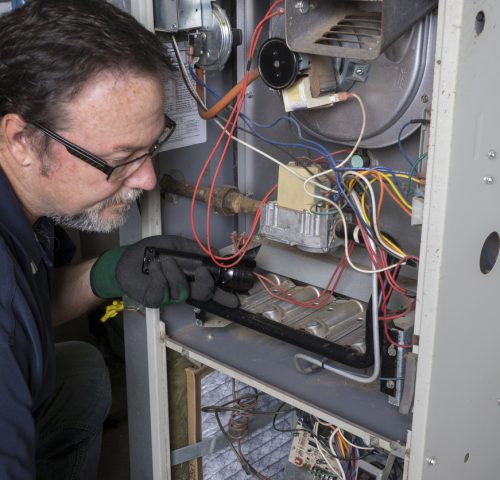 Technician looking over a gas furnace with a flashlight before cleaning it.